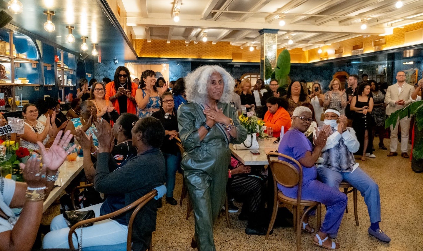 Makani walking through a room full of people who applaud her. Her hands are on her heart in appreciation.