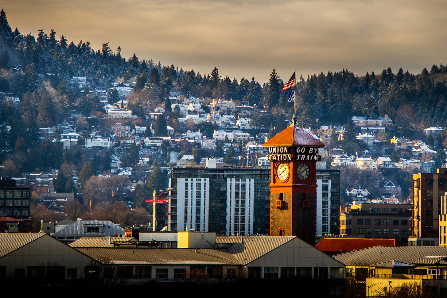 Portland's Union Station clock tower, marked "Go By Train," stands amidst trees and urban architecture.