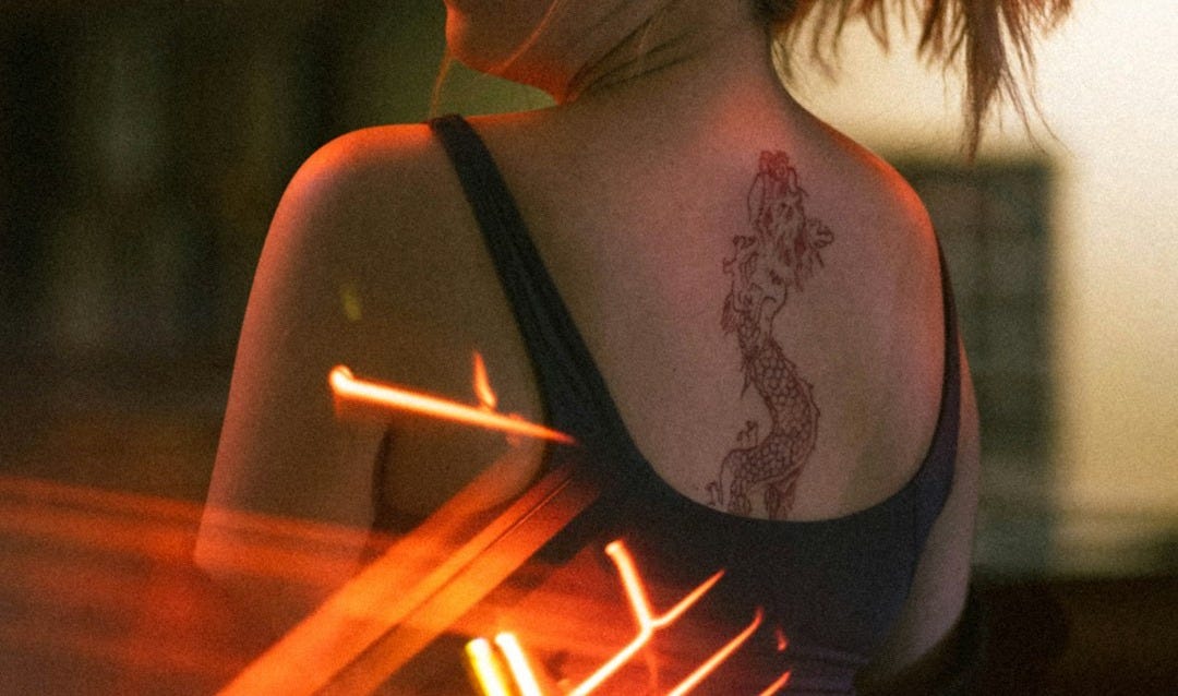 a woman with a tattoo on her back holding a neon sign