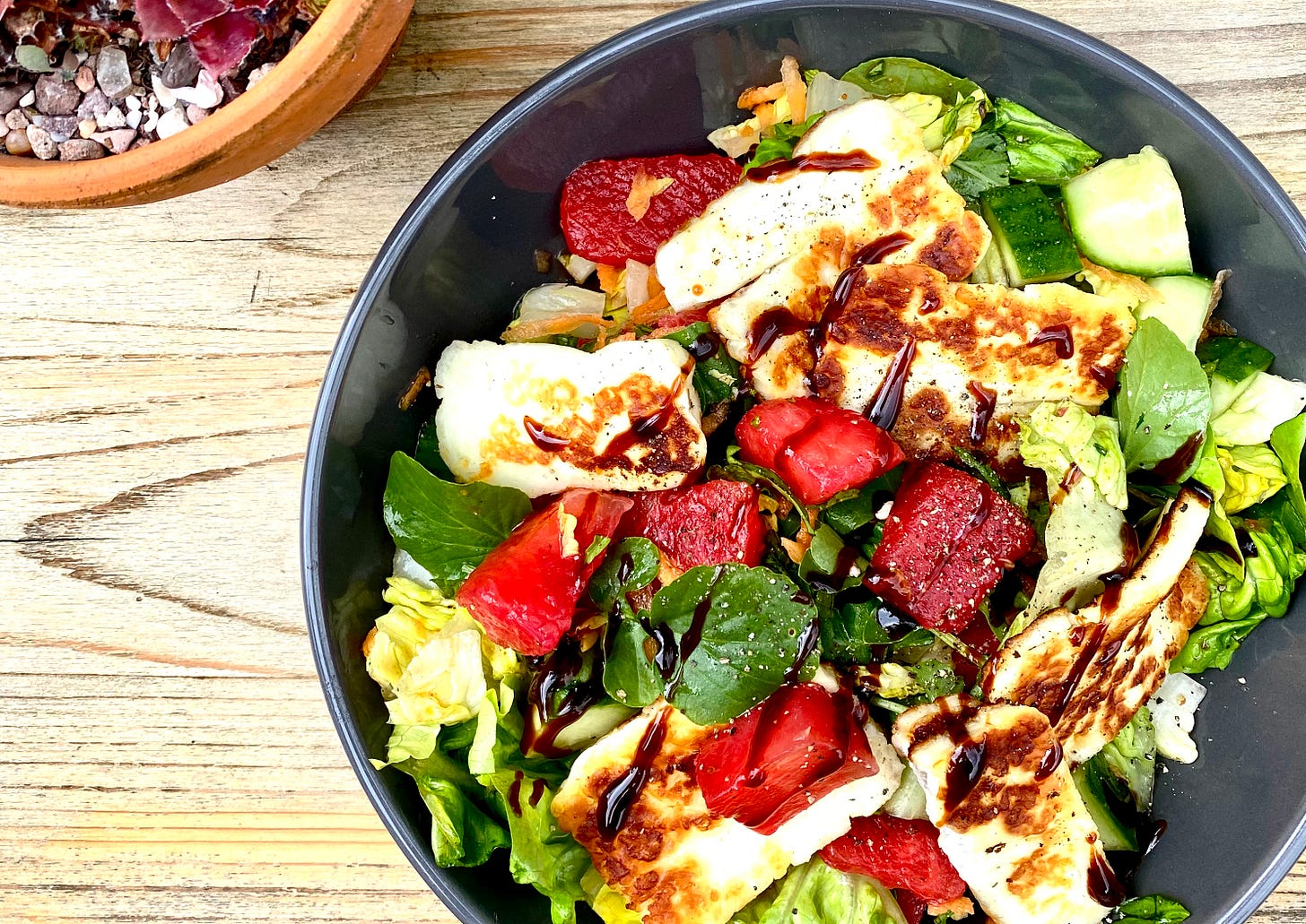 Grey bowl filled with salad of halloumi, watermelon, lettuce, cucumber and carrot, with a drizzle of balsamic glaze.