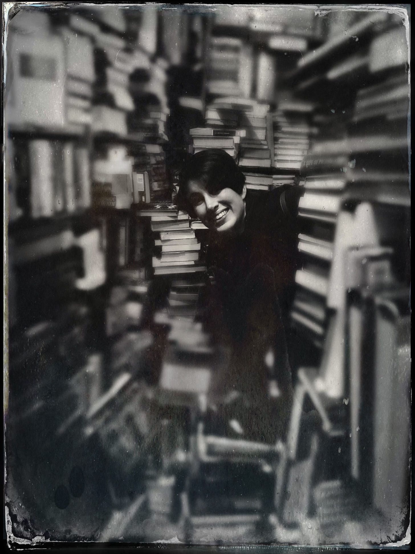 Black-and-white photograph of the author’s wife smiling among shelves of old books inside a New Orleans bookstore.