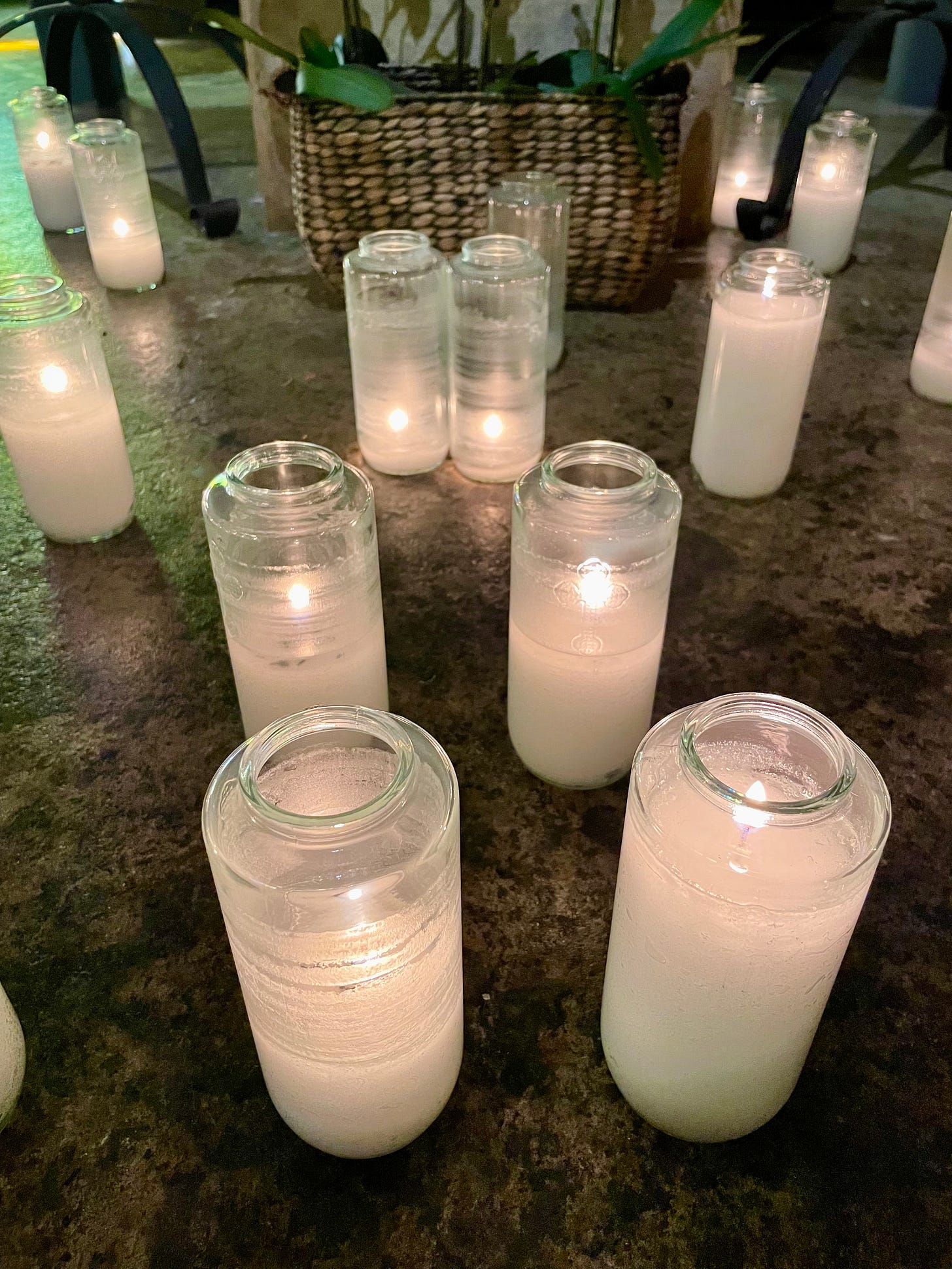 Some 5-day votive candles lit and scattered across a stone floor.