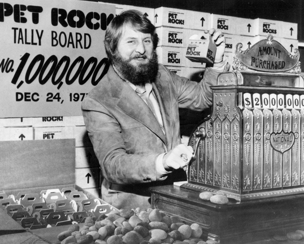 Gary Dahl, creator of the Pet Rock, stands beside a vintage cash register displaying $2,000,000 in sales, holding one of his famous boxed Pet Rocks. Behind him, a tally board marks the sale of the one-millionth Pet Rock on December 24, 1975. Gary Dahl, creator of the Pet Rock, stands beside a vintage cash register displaying $2,000,000 in sales, holding one of his famous boxed Pet Rocks. Behind him, a tally board marks the sale of the one-millionth Pet Rock on December 24, 1975.