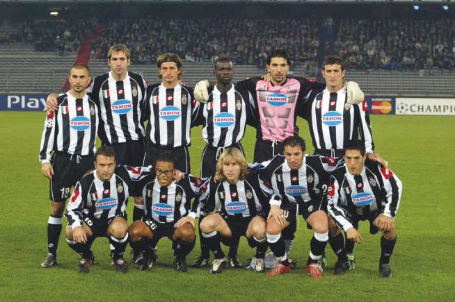 Juventus starting lineup poses in black-and-white TamoiI-sponsored kits with goalkeeper in pink jersey before a Champions League match, mid-2000s.
