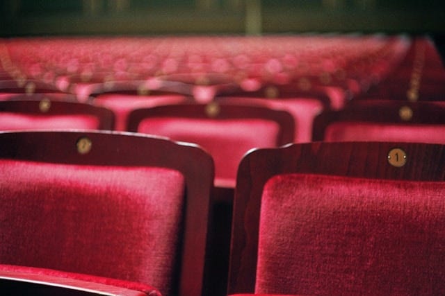 Close-up of a row of red velvet theatre seats, further rows behind in soft focus