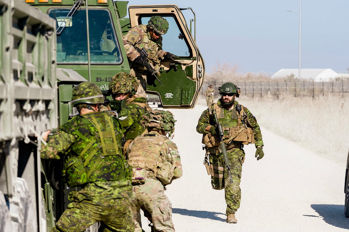 CAF members beside a truck on a road. One member runs with his weapon. CAF members beside a truck on a road. One member runs with his weapon.