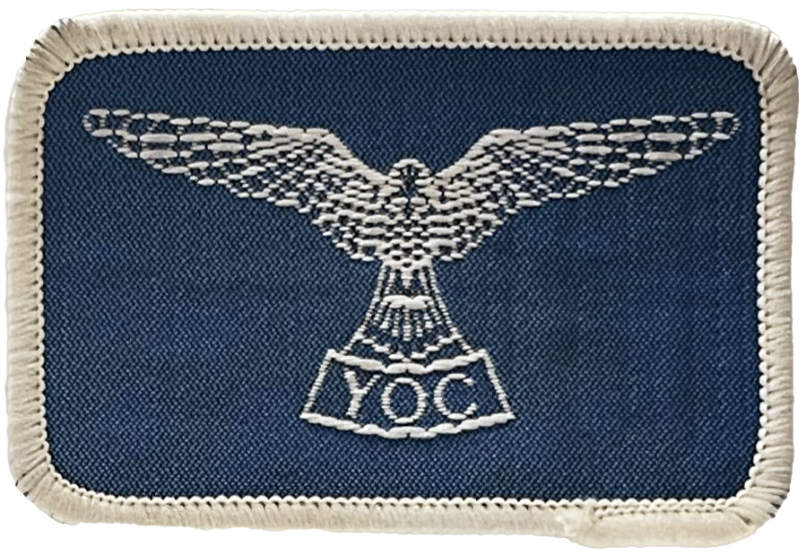 A rectangular blue cloth badge with a bird, wings outstretch embroidered in white with the letters Y.O.C underneath A rectangular blue cloth badge with a bird, wings outstretch embroidered in white with the letters Y.O.C underneath