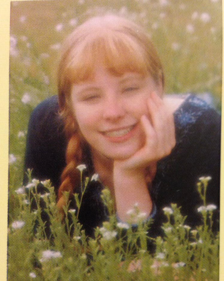 A smiling white teenager in a field with a long braid over her shoulder