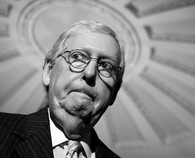 A black-and-white photo of Mitch McConnell seen from below, with a decorative ceiling in the background