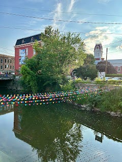 A calm river, showing the reflection of a red brick building, with a string of flags across the water. A calm river, showing the reflection of a red brick building, with a string of flags across the water.