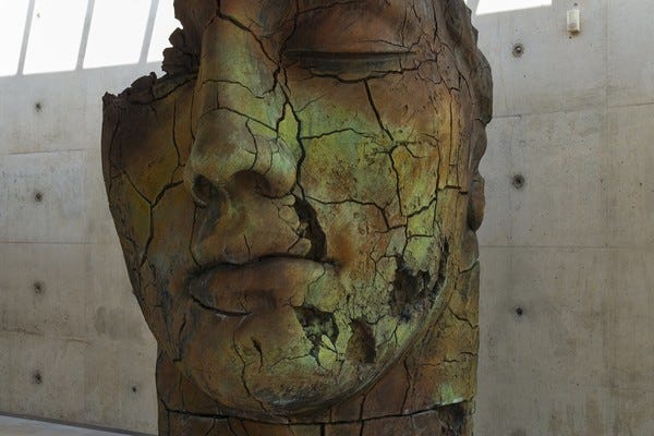 a estátua de coloração amarelo-marrom é grande, do tamanho de uma parede, e mostra a face de um homem (Teseu) repleto de fissuras. Um dos seus olhos caiu com a parte superior da sua cabeça. As pedras no espaço da bochecha, labios e queixo está faltando. O rosto está todo rachado.