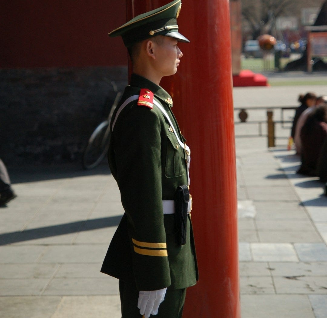 man in green and black camouflage uniform standing near red wall during daytime