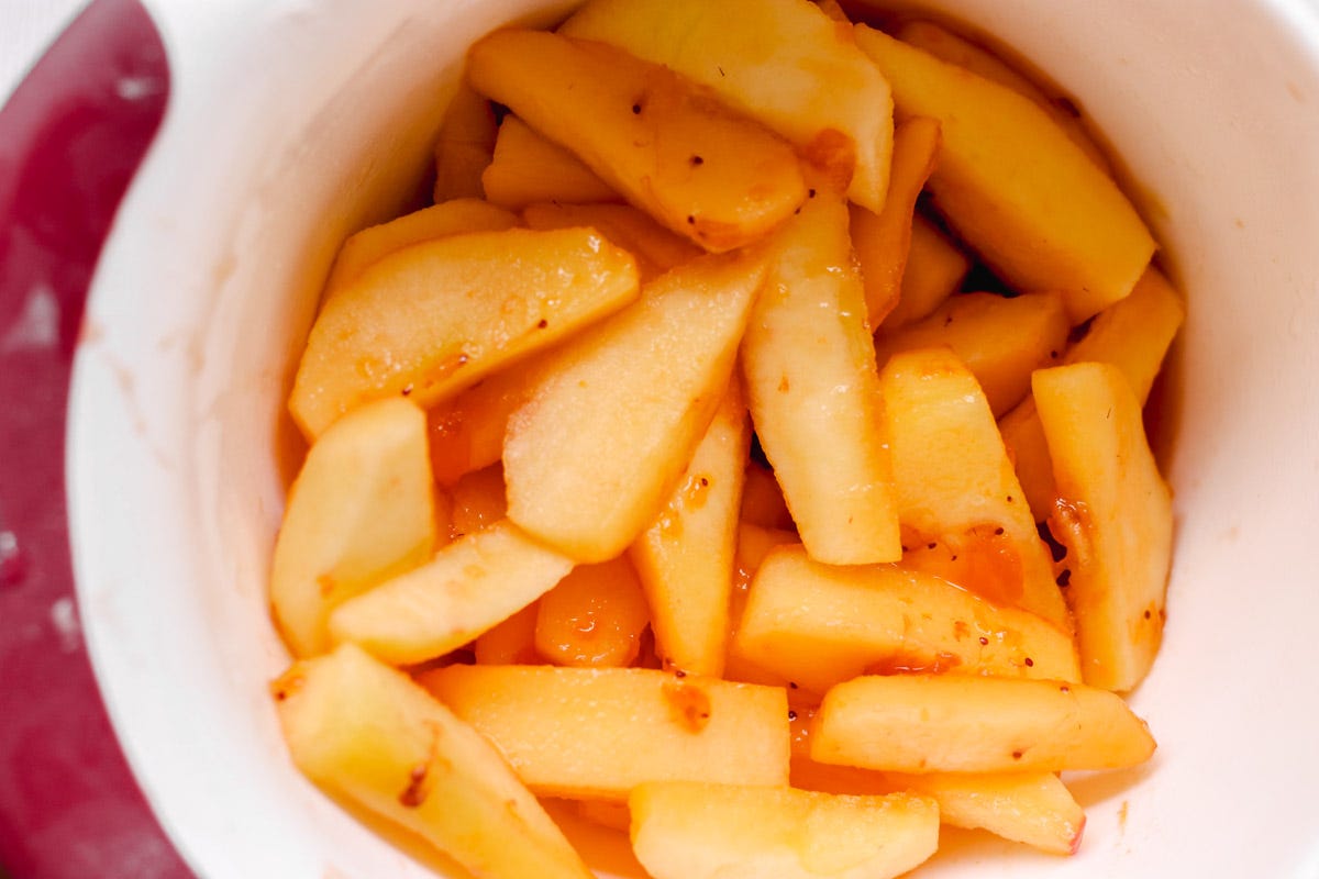 close up image of sliced apples in a white mixing bowl. 