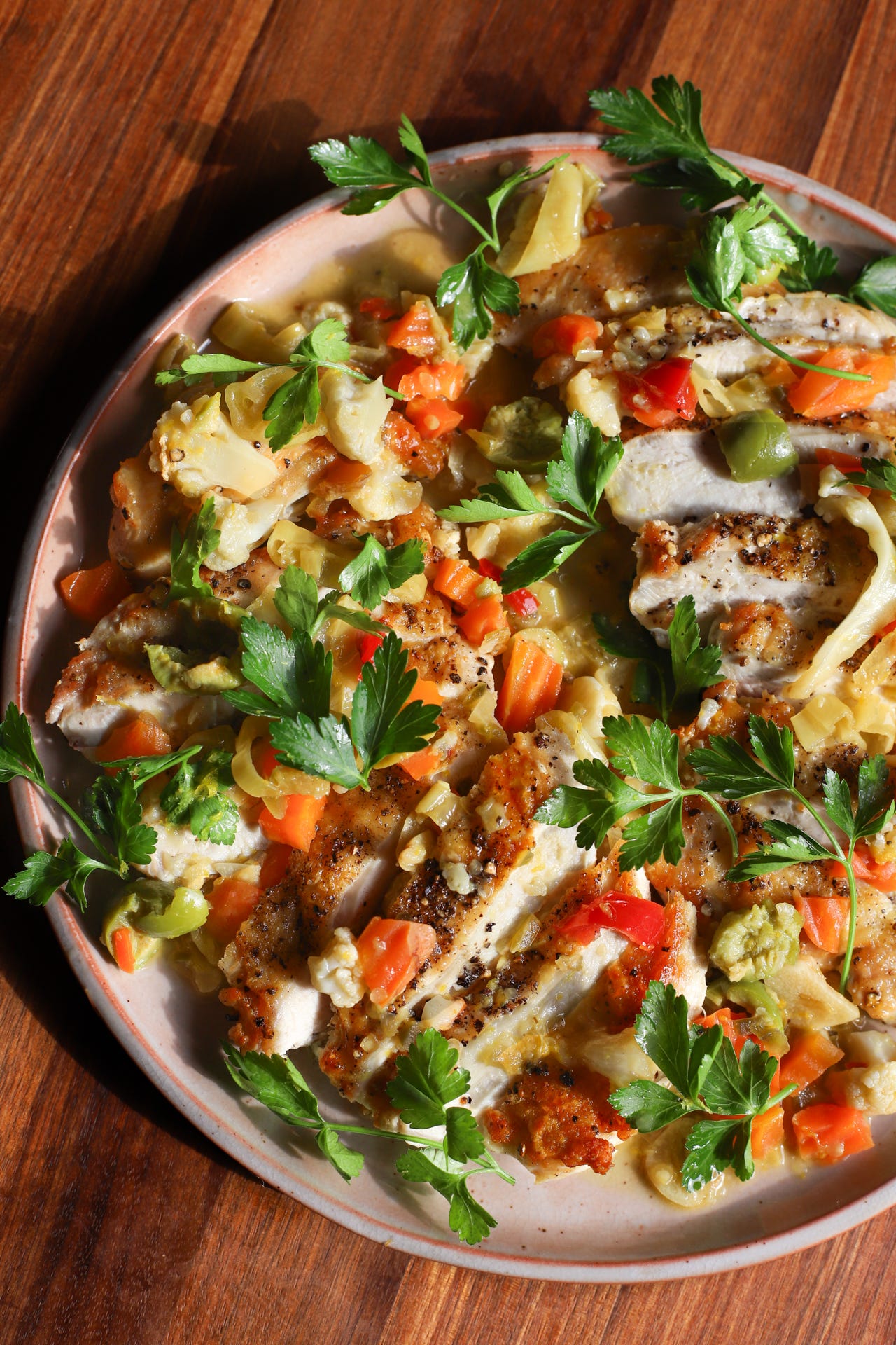 Plate with sliced crispy-skinned chicken breast and chopped pickled Italian vegetables with parsley leaves