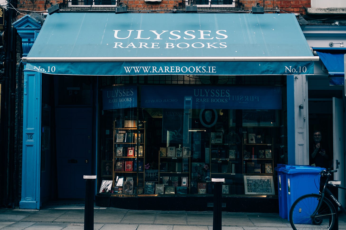 The blue-painted shopfront of Ulysses Rare Books in Dublin, its window packed with secondhand books, a bicycle and a blue recycling bin on the pavement outside. The blue-painted shopfront of Ulysses Rare Books in Dublin, its window packed with secondhand books, a bicycle and a blue recycling bin on the pavement outside.