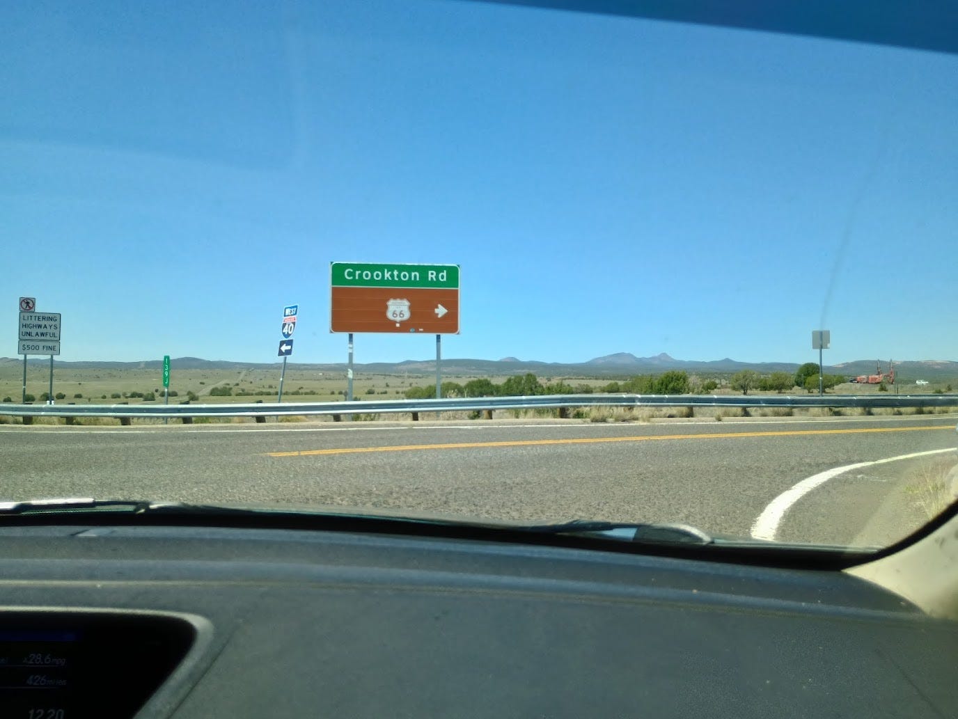 View of intersection at top of freway off-ramp, including signs pointing to Historic Route 66, desert, mountains