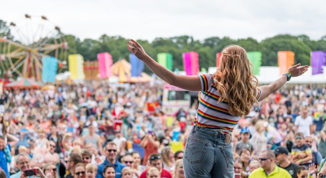 A stage with a woman wearing a t-shirt and jeans holding her arms out, and a crowd of people in front of her