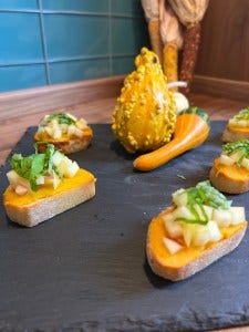 Butternut Squash Crostini topped with Apple and Basil on a black slate tray with decorative gourds. Butternut Squash Crostini topped with Apple and Basil on a black slate tray with decorative gourds.