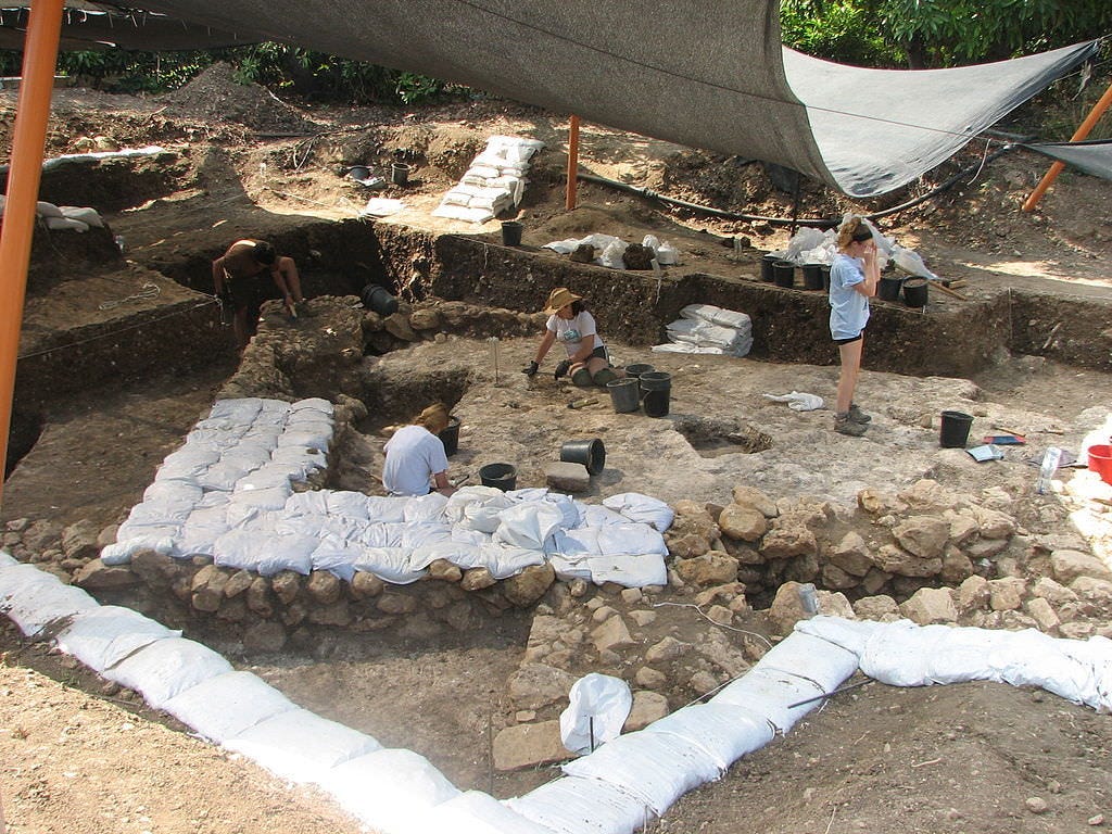 People at a dig with layers of stones outlining walls covered carefully with white plastic sandbags. People at a dig with layers of stones outlining walls covered carefully with white plastic sandbags.