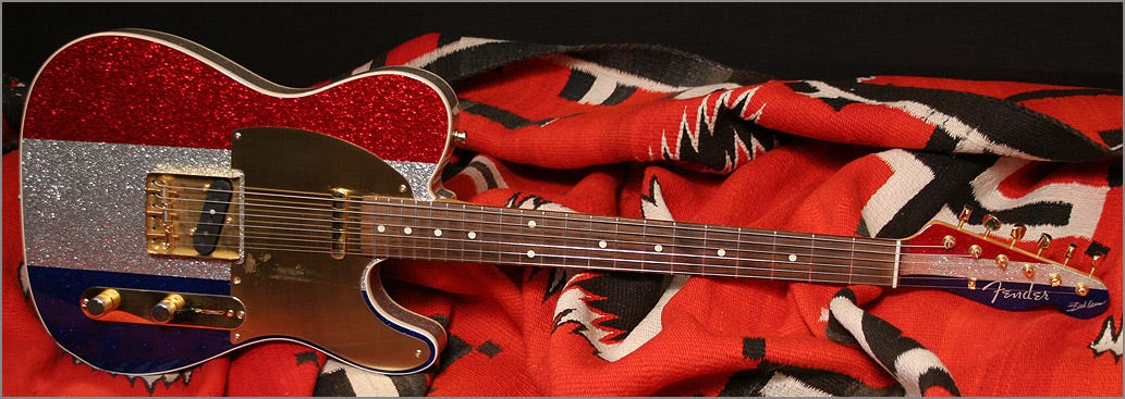 A patriotic guitar with red, white, and blue paint, featuring a 98 Fender Buck Owens steel guitar.