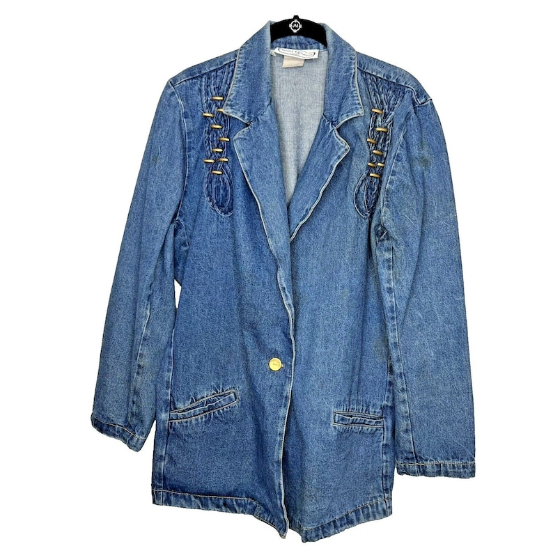 May include: A blue denim jacket with gold buttons and stitching detail. The jacket has a collar, long sleeves, and two pockets on the front. The jacket is unbuttoned and the inside is not visible.