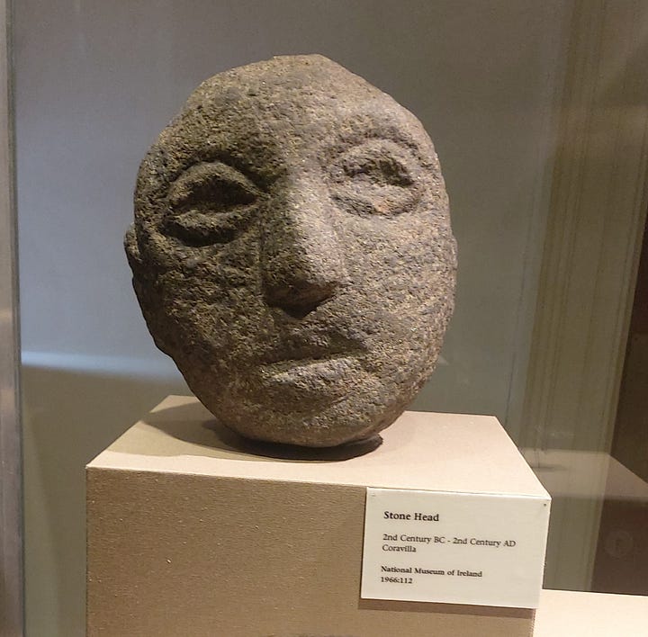 Two faces of the Corleck head on the top row with an image of a stamp featuring the Corleck head between them. Two images of other stone heads on display in our museum. All of them are made of a greyish-brown grainy stone, their facial features minimally represented and expressionless.