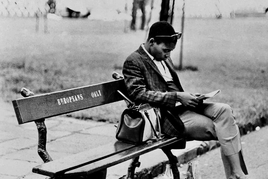 A black and white photo of a Black man sitting on a bench labelled "Europeans only".