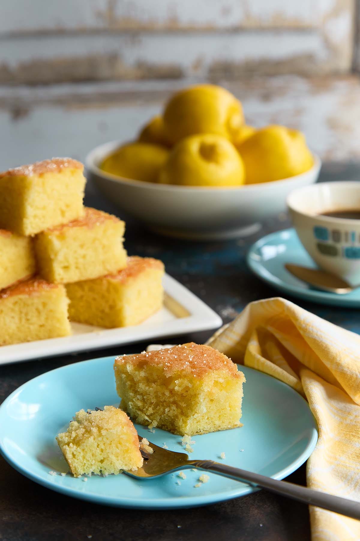 A close-up of a moist Lemon Drizzle Cake slice showing a fine crumb, topped with a crunchy, crackled sugar and lemon juice glaze.
