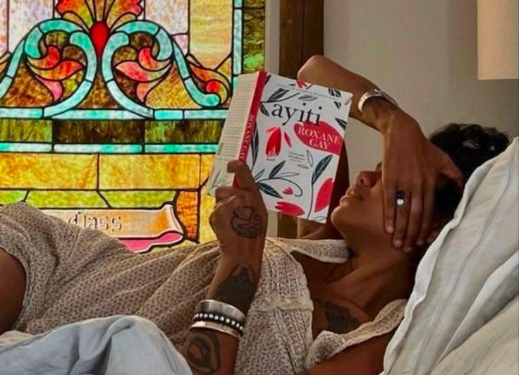 This may contain: a woman laying in bed reading a book with a stained glass window behind her on the wall This may contain: a woman laying in bed reading a book with a stained glass window behind her on the wall