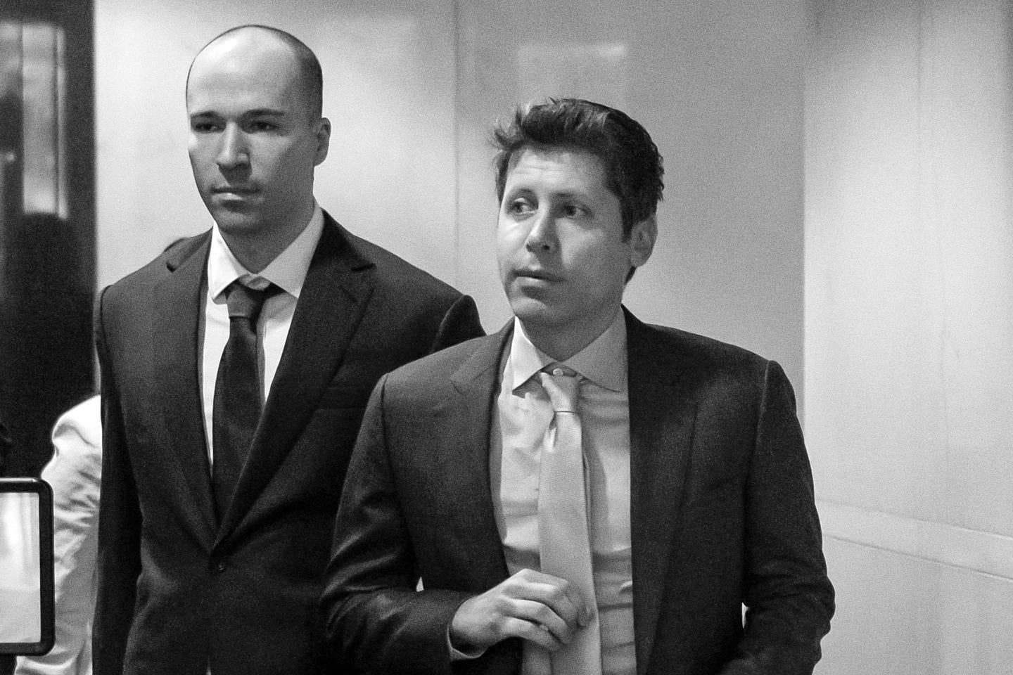 OpenAI cofounder and president Greg Brockman (left) and cofounder and CEO Sam Altman (right) dressed in suits and walking through the lobby of a court house.