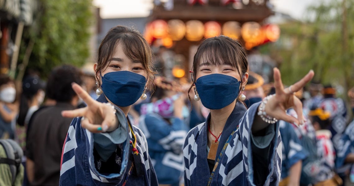 two ladies showing the peace sign, with a festival float behind them