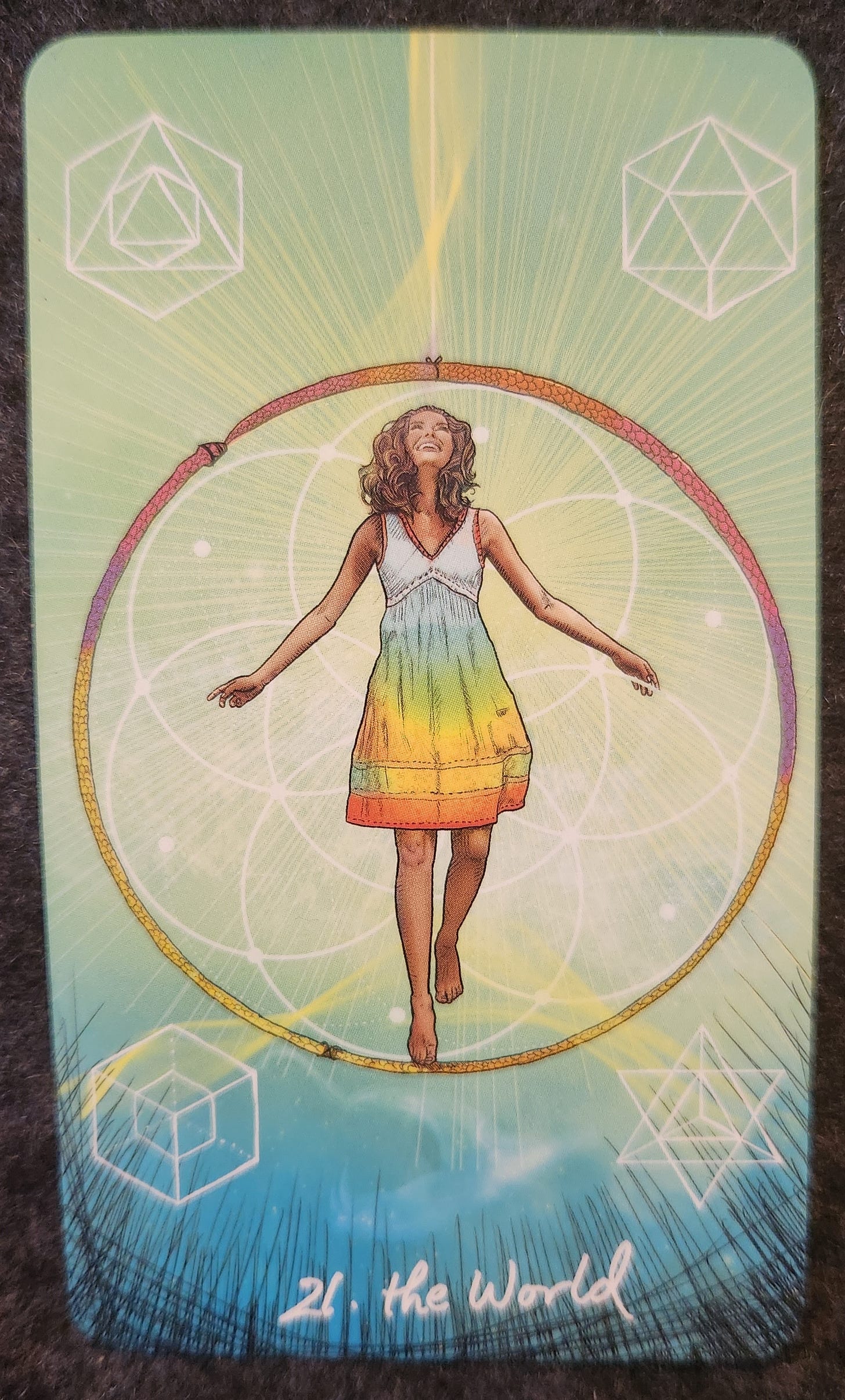 A tarot card labelled 22. The World. A woman is standing with her arms open and face tilted upwards. She is in the middle of a ring that resembles a snake biting its own tail. Behind her are geometric shapes etched into the sky. 