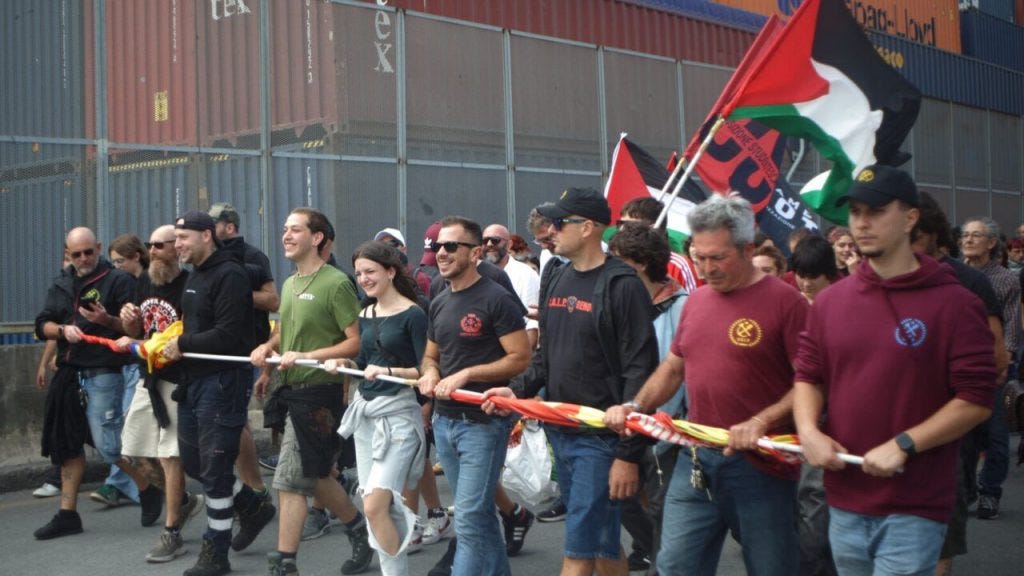Dock workers marching together with banners and sticks and Palestine flags.