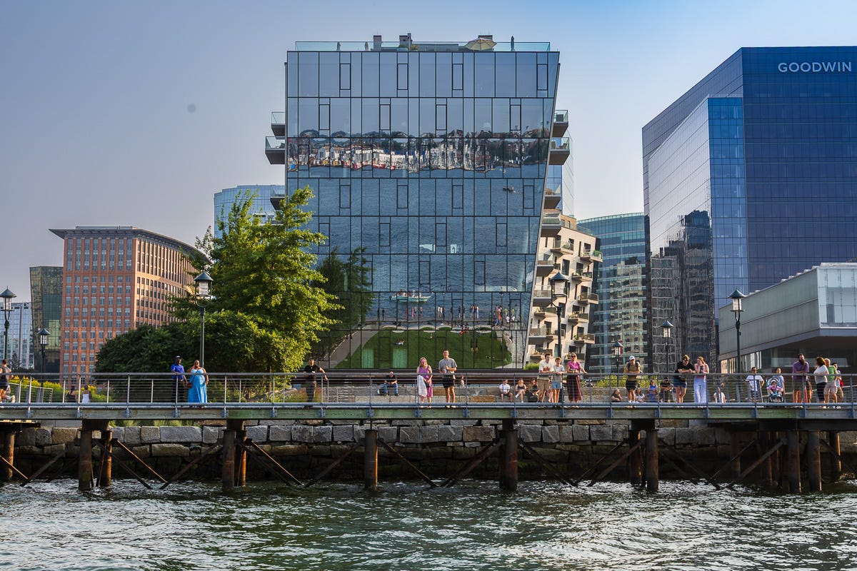 Modern glass building reflecting harbor views with people walking along the pier in Boston Harbor