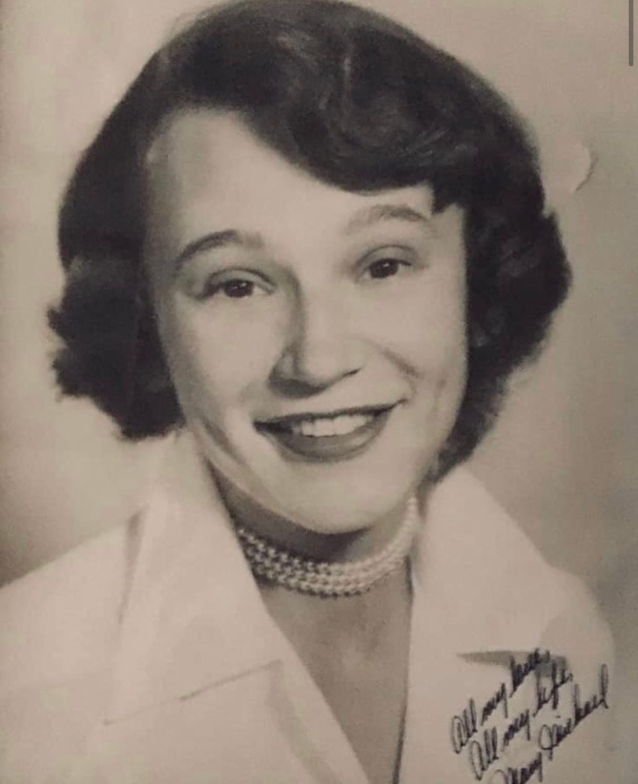 Black-and-white studio portrait of Mary Michael Fiorella, smiling, in a white collared blouse and pearl choker, signed in ink Black-and-white studio portrait of Mary Michael Fiorella, smiling, in a white collared blouse and pearl choker, signed in ink