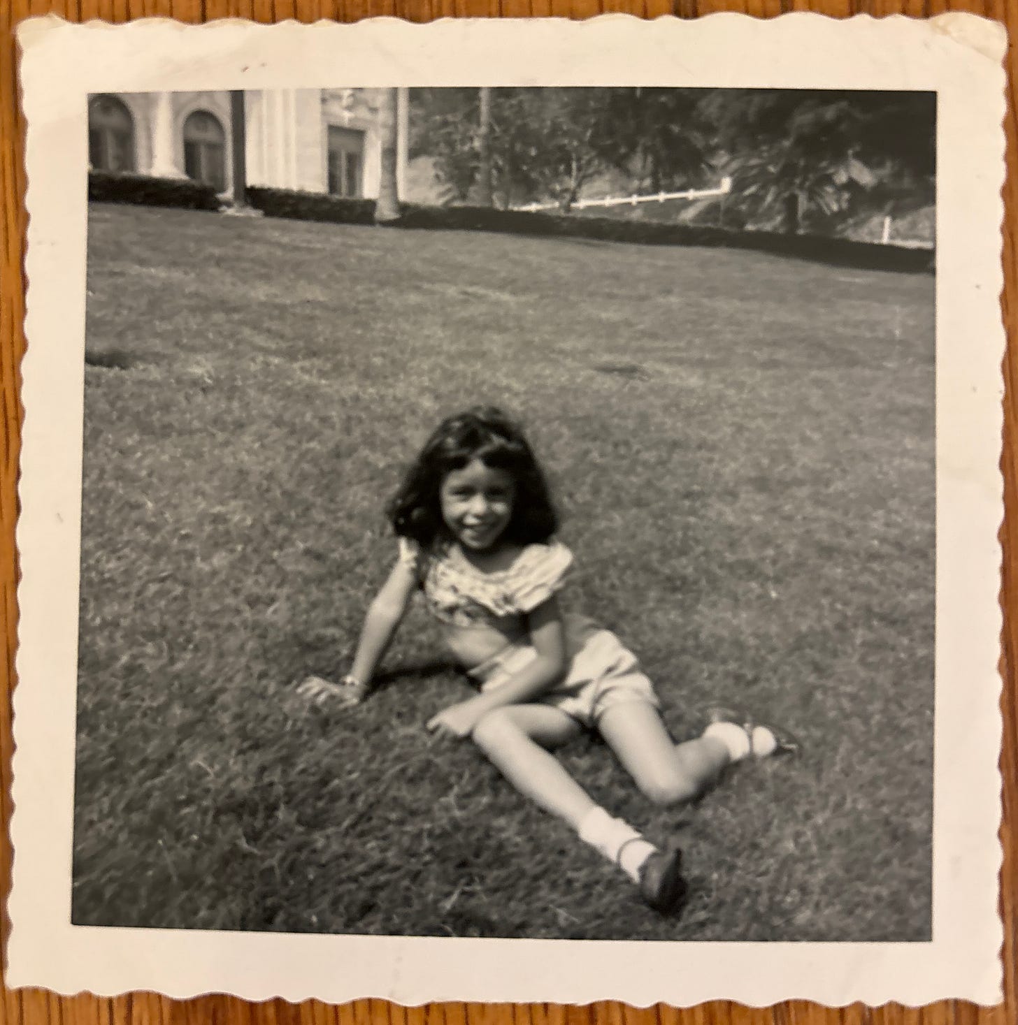 Photo of girl with dark hair sitting on grass lawn.