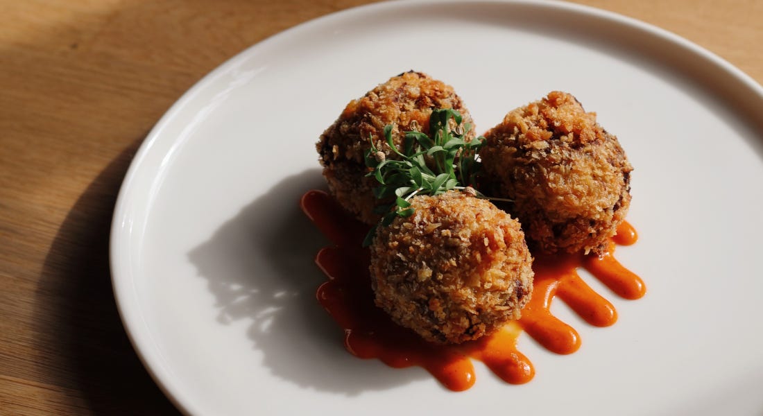 A white plate of venison croquettes with orange sauce on them, on top of a wooden table