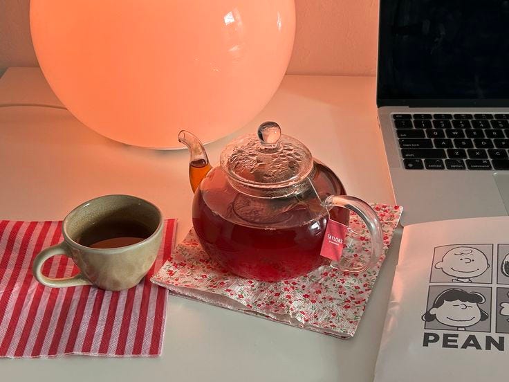This may contain: a tea pot and cup sit on a napkin next to a laptop