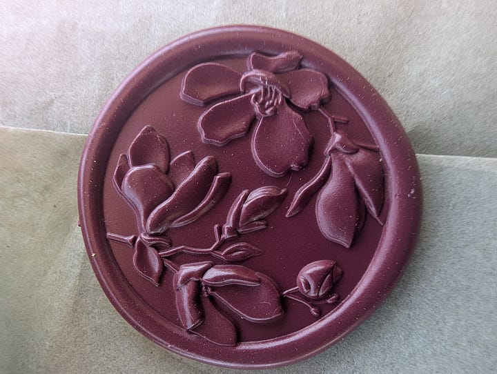 Images of the contents of a packaged labeled "Women at the Edge of the Woods." The package is sealed with a red wax seal. Inside there are colored pencils, a journal and a spiral-bound workbook.