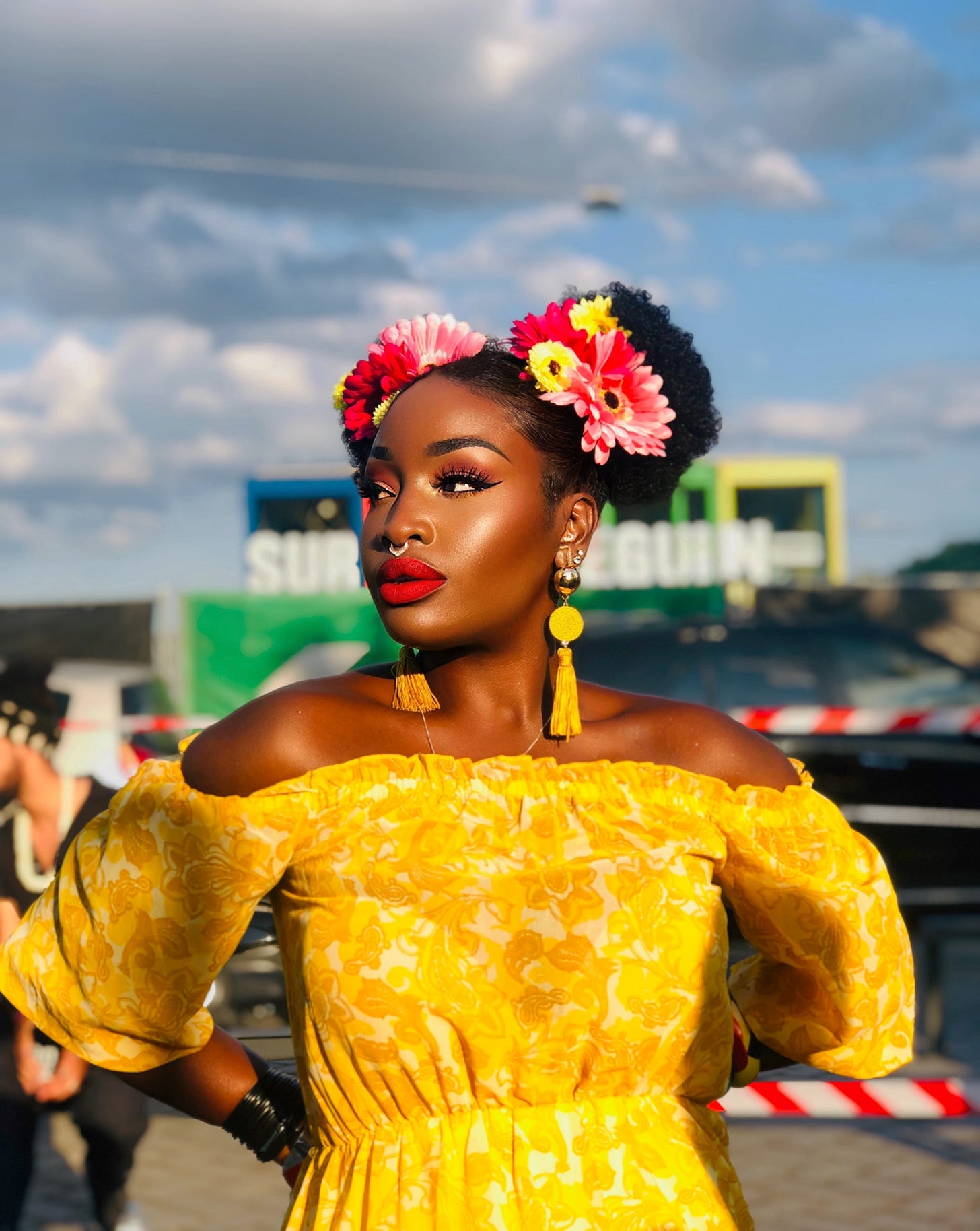 Portrait of Lovette Jallow, autistic author and activist, standing in golden light with flowers in her hair and a steady, unsmiling gaze. Captures the tension between visibility and interior labor. Portrait of Lovette Jallow, autistic author and activist, standing in golden light with flowers in her hair and a steady, unsmiling gaze. Captures the tension between visibility and interior labor.