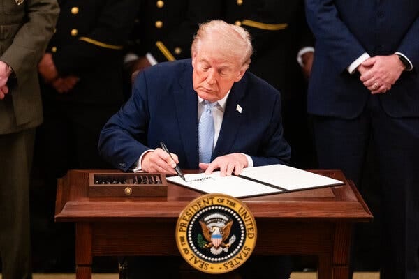 President Trump signing a document at a wooden desk. President Trump signing a document at a wooden desk.