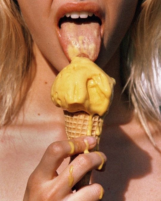 This may contain: a woman eating an ice cream cone with yellow icing on her face and mouth