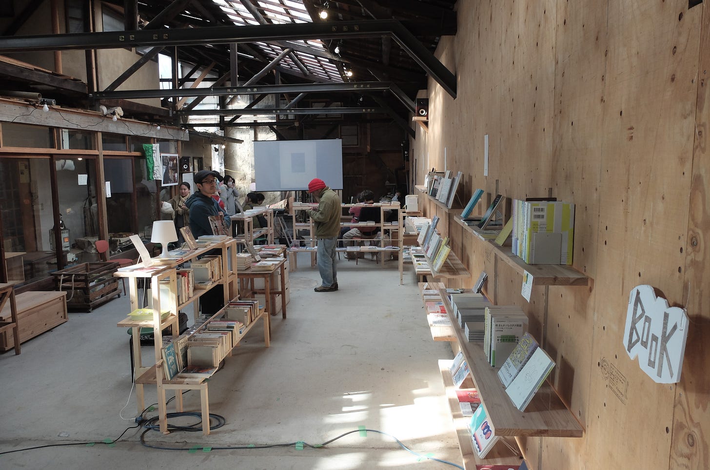 イベント会場の様子。手前に木製の本棚があって、陳列された本を手に取って読んでいる人が写っている。