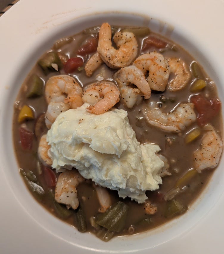 A bowl of gumbo topped with shrimp and potato salad