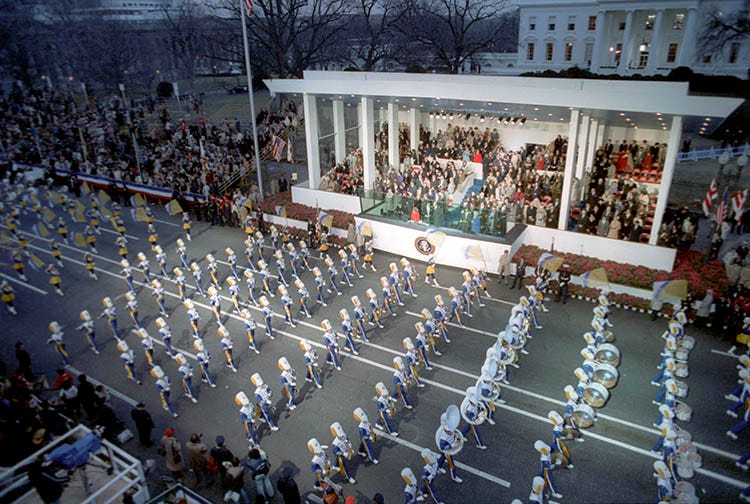1981: marching band passes the presidential reviewing stand with dignitaries and the president and his wife. It is a cold January 20th and everyone is bundled up against the cold.
