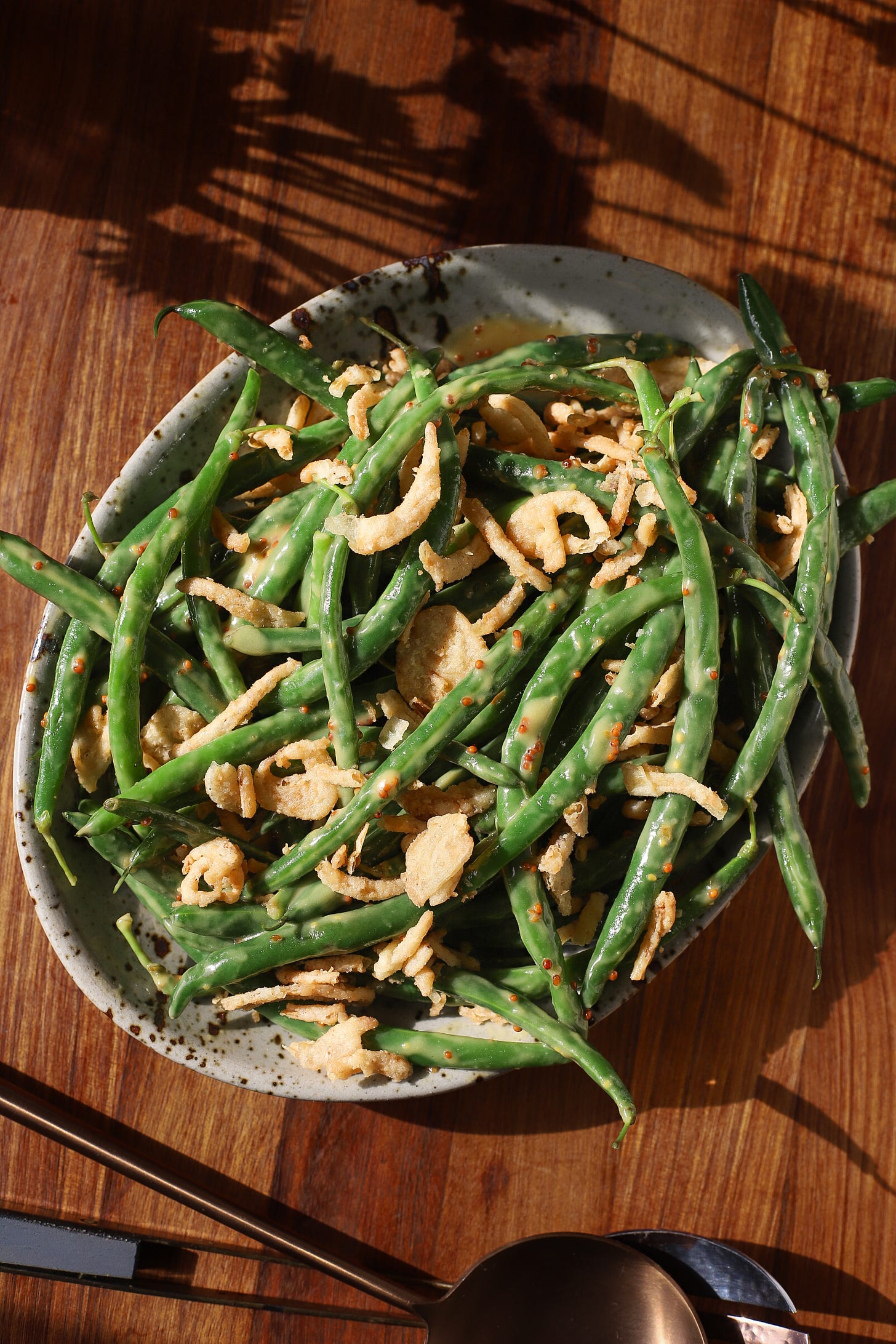 Wood table with plate of green beans tossed in garlic-mustard dressing and topped with fried onions
