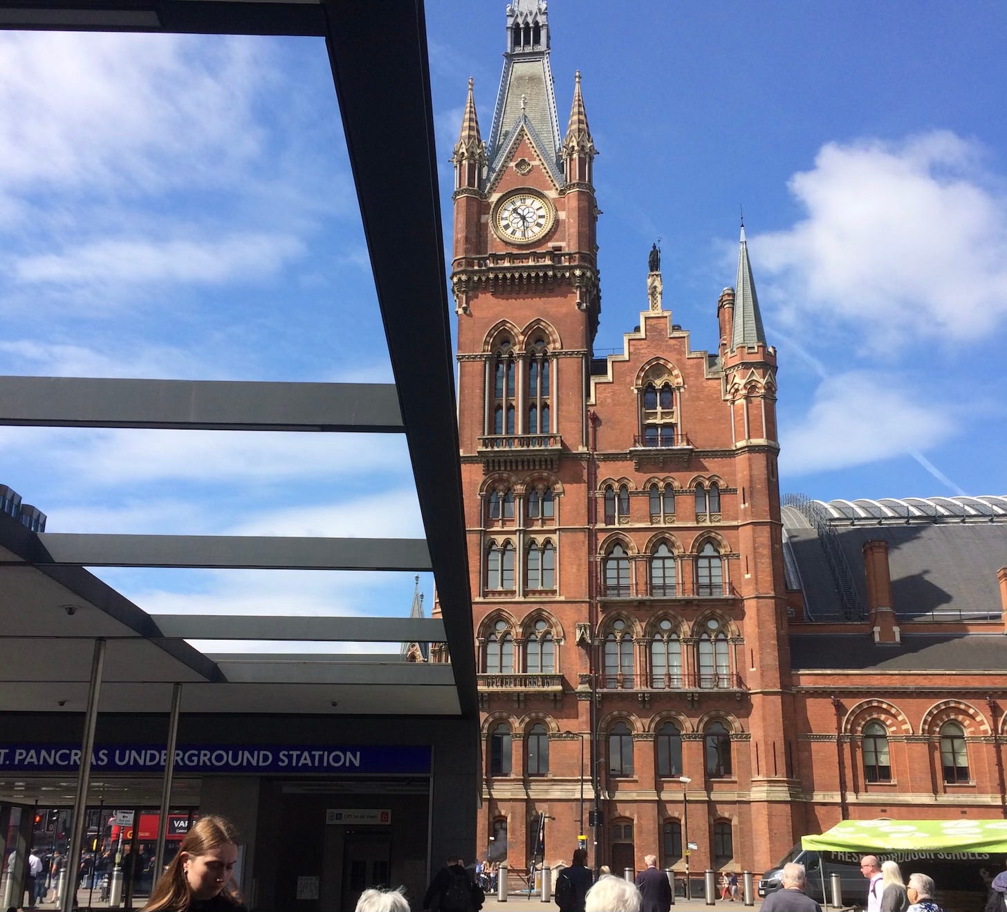 A red brick building in London with tall clock tower seen from the ground against a blue sky.