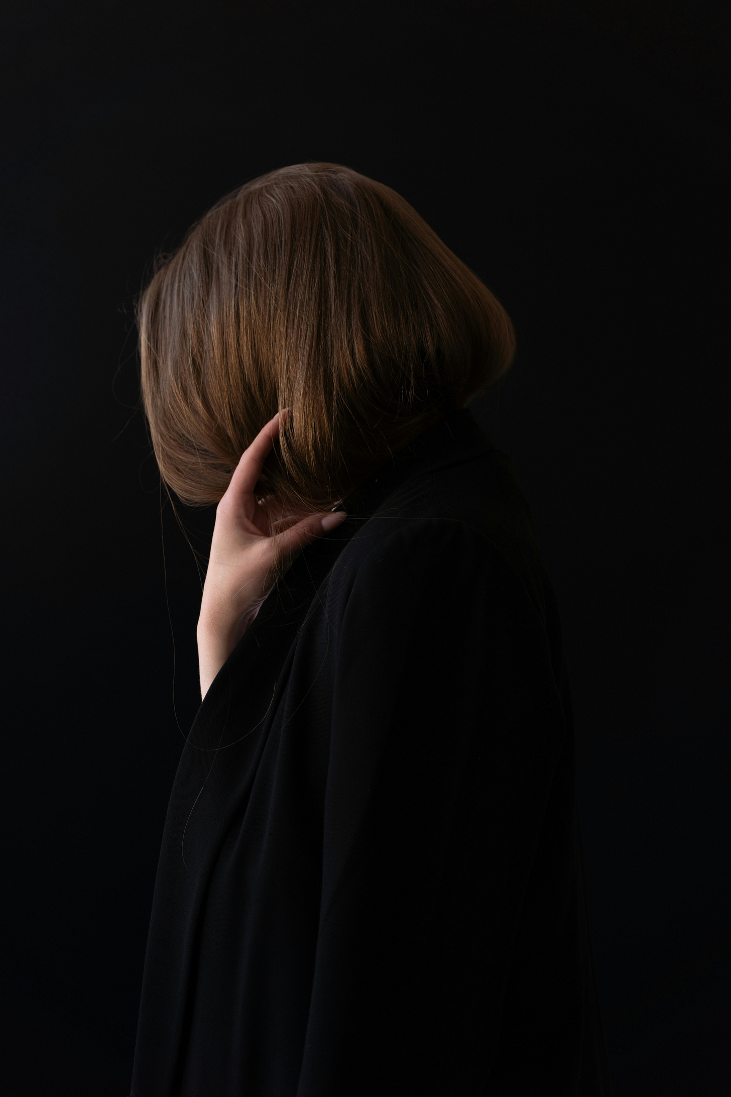 a woman with a bob haircut is seen from the side, with her hand up and face hidden by the hair.