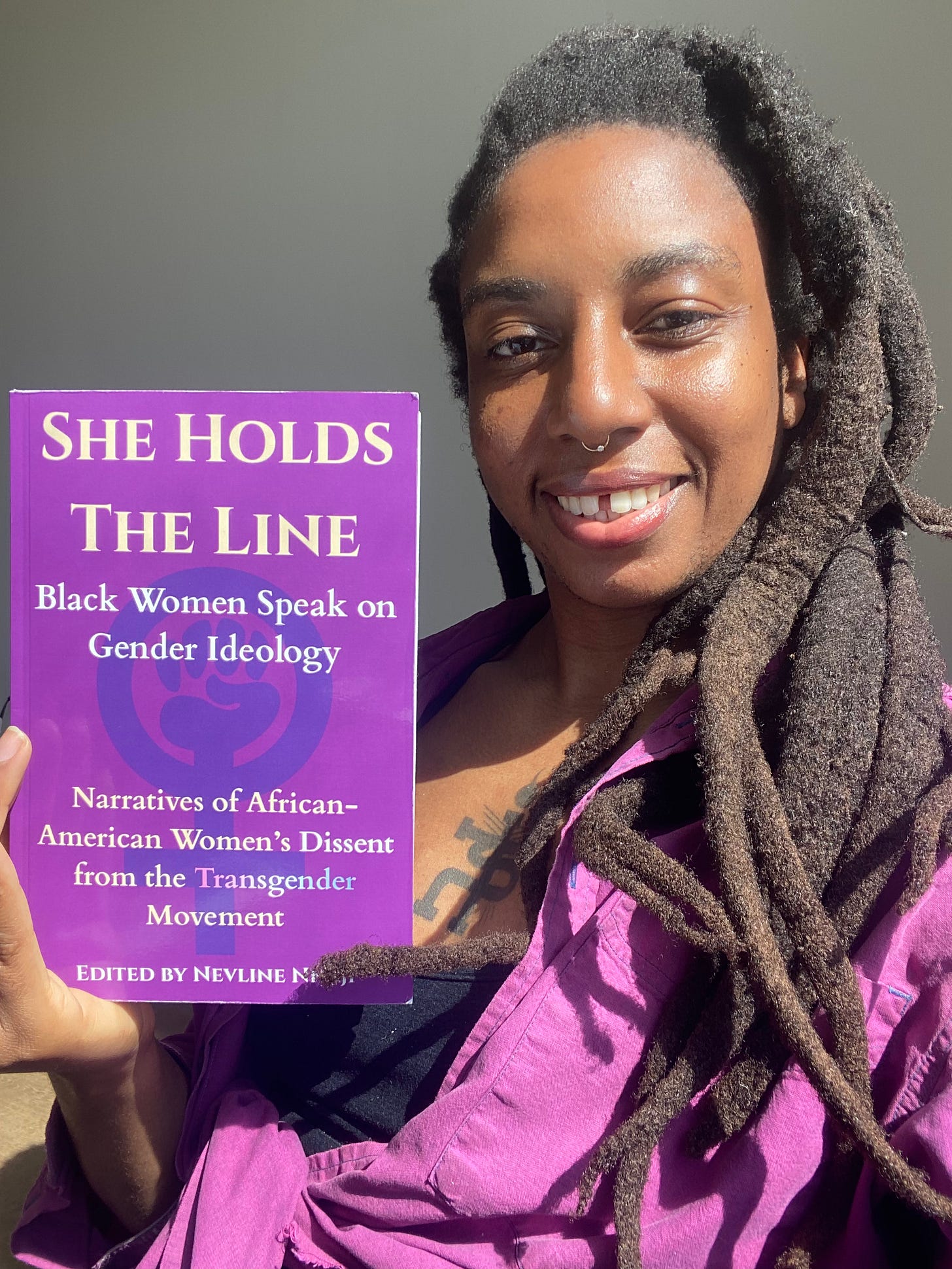 beautiful n3vlynnn holding a copy of her anthology, "She Holds The Line: Black women speak on gender ideology"