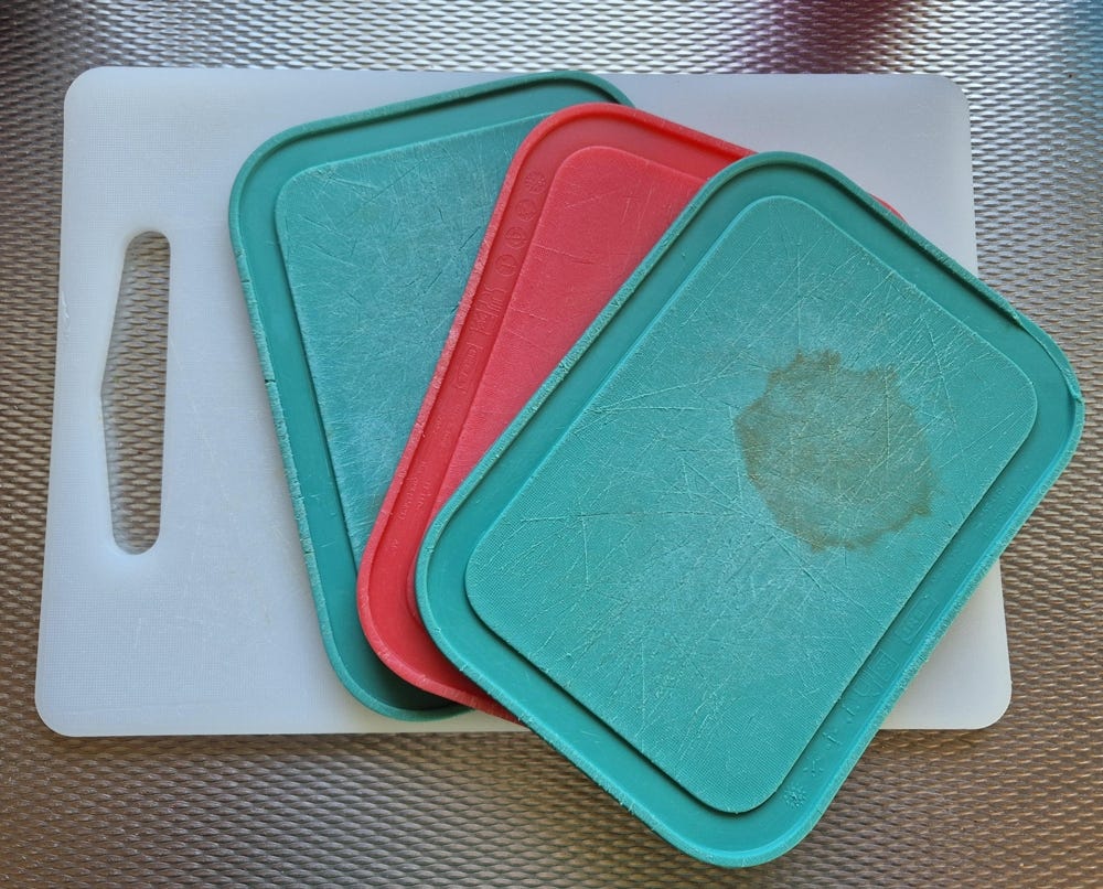 Large white cutting board with 2 small green and 1 red cutting board on top of it. All sit on a silver countertop.